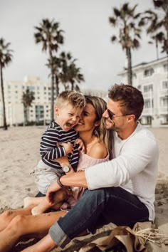 a man, woman and child are sitting on the beach with palm trees in the background