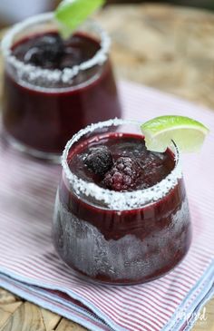 two glasses filled with liquid and garnished with lime wedges on a table