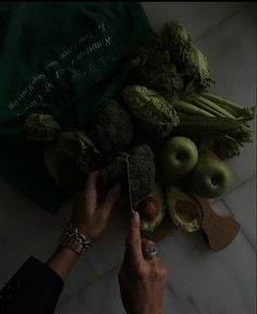 a person cutting broccoli on top of a table with other fruits and vegetables