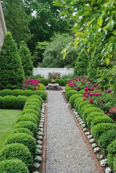 a garden with lots of green plants and flowers in the center, surrounded by gravel path