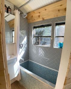 the inside of a tiny bathroom with blue and white tiles on the walls, windows, and bathtub