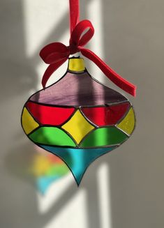 a stained glass ornament hanging from a red ribbon on a white wall with sunlight coming through the window