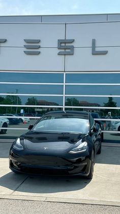 a black car is parked in front of a tesla dealership with other cars behind it