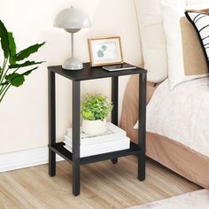 a small black end table with a potted plant next to it on a bed