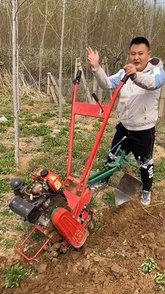 a man standing next to a red plow in the middle of a dirt field