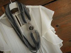 a woman's white shirt and gray scarf on a hanger next to a wooden wall