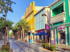 an empty street with colorful buildings and palm trees on both sides in front of the train tracks