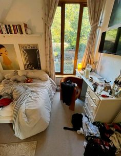 an unmade bed sitting in a bedroom next to a dresser and tv on top of it