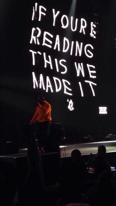 a man standing on top of a stage next to a sign that says if you're reading this we made it