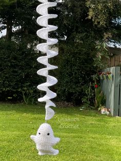 a white plastic fish decoration hanging from a pole in the grass with trees and bushes behind it