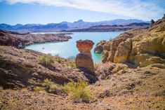 a large body of water surrounded by rocky hills and desert land with mountains in the background