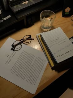 two books and glasses are sitting on a desk next to a glass with water in it