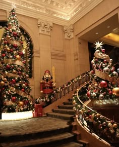 christmas trees and decorations are on display in the foyer of a building with ornately decorated staircases