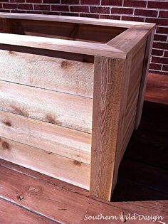 a wooden planter sitting on top of a wooden floor next to a brick wall