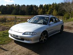 a silver car parked on the side of a dirt road next to a lush green field