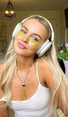 a woman with yellow patches on her face and headphones around her neck, wearing white tank top