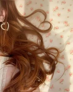 a woman with long red hair laying on top of a flowery bed covered in white sheets