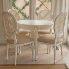 a white table and four chairs in front of a large window with vines on it