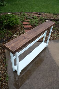 a wooden bench sitting on top of a cement walkway next to grass and bushes in the background