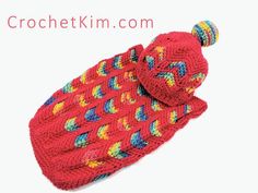 a crocheted red hat with multicolored feathers on it