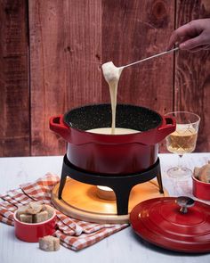 a person is pouring something into a fonding pot on a table with other dishes