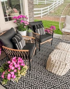 two black chairs sitting on top of a rug in front of a white house with pink flowers