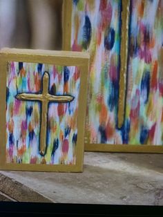 two small wooden crosses sitting next to each other on top of a table in front of paintings