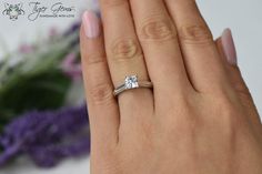 a woman's hand with a diamond ring on her finger and purple flowers in the background