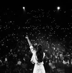 a woman standing on top of a stage holding her arms up in the air while surrounded by people