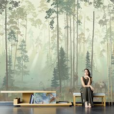 a woman sitting on a bench in front of a forest mural