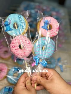 a person is holding three donuts with blue frosting and pink sprinkles