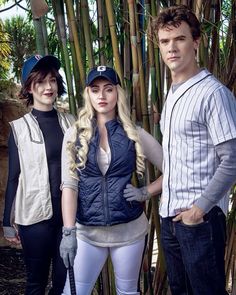 three people standing next to each other in front of some bamboo trees with baseball caps on