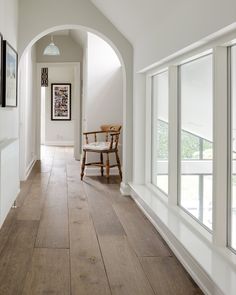 an arched hallway with wood floors and white walls, along with framed pictures on the wall