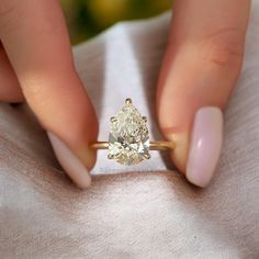 a woman's hand holding an engagement ring with a pear shaped diamond on it