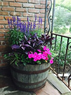 a wooden barrel filled with purple flowers next to a brick wall and wrought iron railing