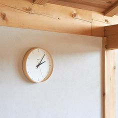 a clock mounted to the side of a wall next to a wooden beam and window