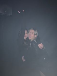 two people standing in the dark with their arms around each other and one person covering his face