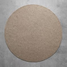 a round rug is shown on the floor in front of a concrete wall with a plant