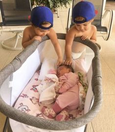 two babies are playing in a crib with hats on and one is laying down