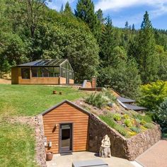 a small house with a green roof in the middle of some trees and grass on top of it