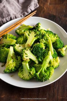 a white plate topped with broccoli and chopsticks on top of a wooden table