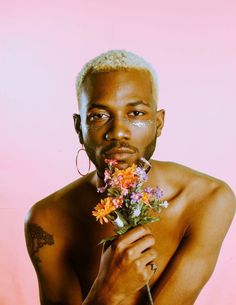 a shirtless man holding flowers in front of his face and looking at the camera