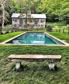 a stone bench sitting in front of a pool surrounded by lush green grass and trees