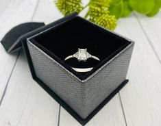 an engagement ring in a box on a white wooden table next to some green plants