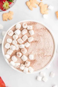 hot chocolate with marshmallows in a white bowl surrounded by cut up cookies and strawberries