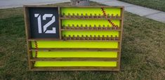 a wooden shelf with baseballs and numbers on it in the grass next to a tree