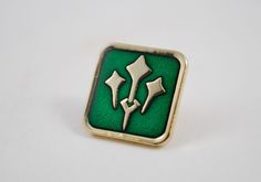 a green and gold colored square shaped pin