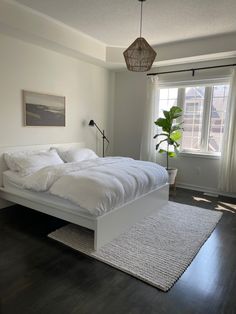 a white bed sitting next to a window in a bedroom on top of a hard wood floor