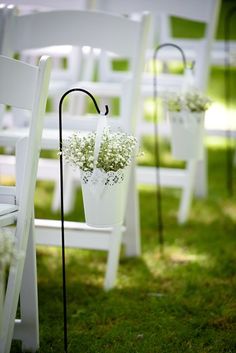 white chairs are lined up on the grass with flowers in buckets attached to them