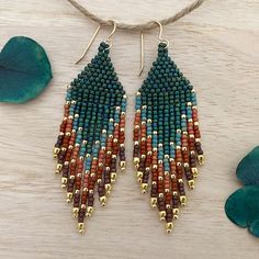 a pair of beaded earrings sitting on top of a wooden table next to green leaves